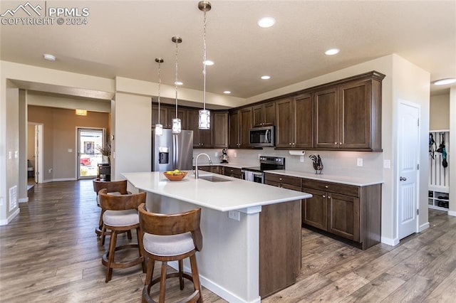 kitchen with hanging light fixtures, stainless steel appliances, wood-type flooring, dark brown cabinetry, and sink