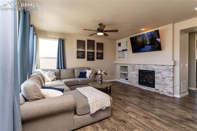 living room with ceiling fan, a stone fireplace, dark hardwood / wood-style floors, and built in shelves