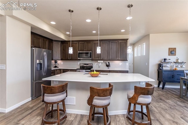 kitchen with appliances with stainless steel finishes, a kitchen bar, pendant lighting, and an island with sink