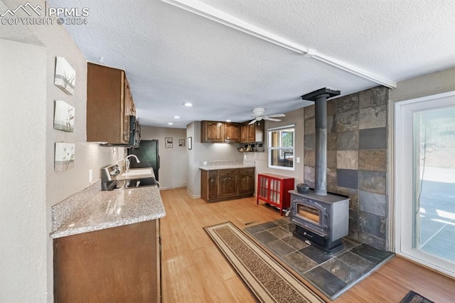 kitchen with light wood-type flooring, tile walls, ceiling fan, and a wood stove