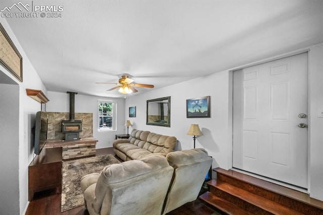 living room featuring dark wood-type flooring, ceiling fan, and a wood stove