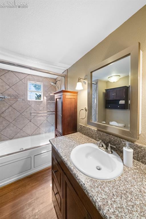 bathroom with wood-type flooring, vanity, and tiled shower / bath