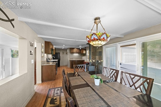 dining space with a textured ceiling, light hardwood / wood-style flooring, sink, and beam ceiling