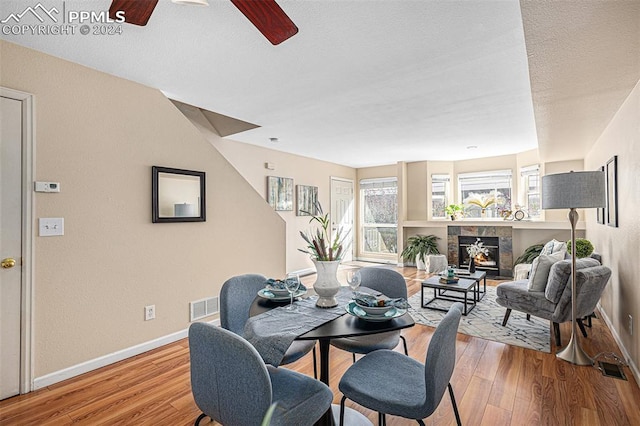 dining room featuring light hardwood / wood-style flooring, ceiling fan, a fireplace, and a textured ceiling