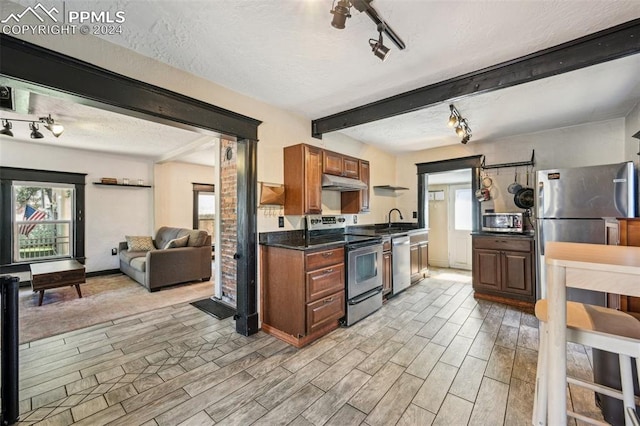 kitchen featuring beamed ceiling, appliances with stainless steel finishes, light wood-type flooring, and a wealth of natural light