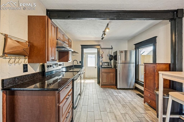 kitchen featuring dark stone counters, stainless steel appliances, a textured ceiling, and light wood-type flooring