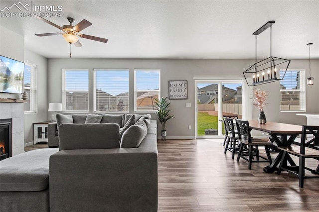 living room featuring a textured ceiling, ceiling fan with notable chandelier, a fireplace, and dark hardwood / wood-style floors