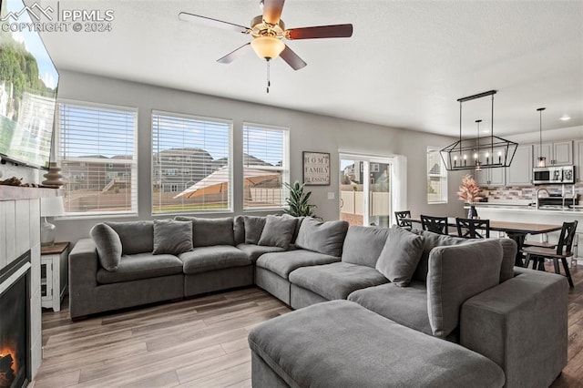 living room featuring ceiling fan with notable chandelier and light hardwood / wood-style flooring