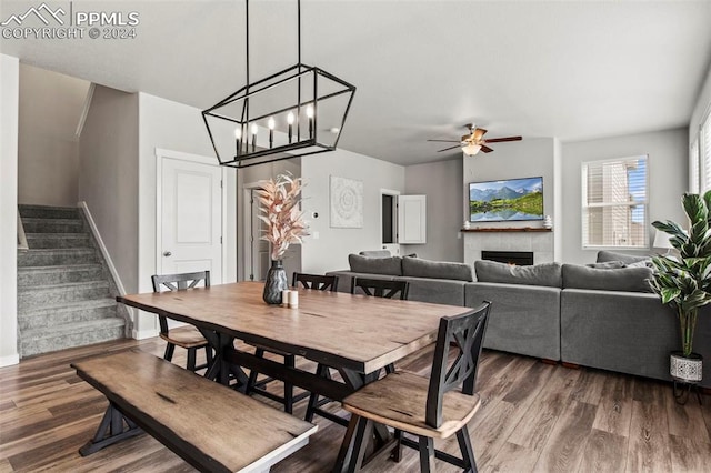 dining room with ceiling fan with notable chandelier, wood-type flooring, and a tile fireplace