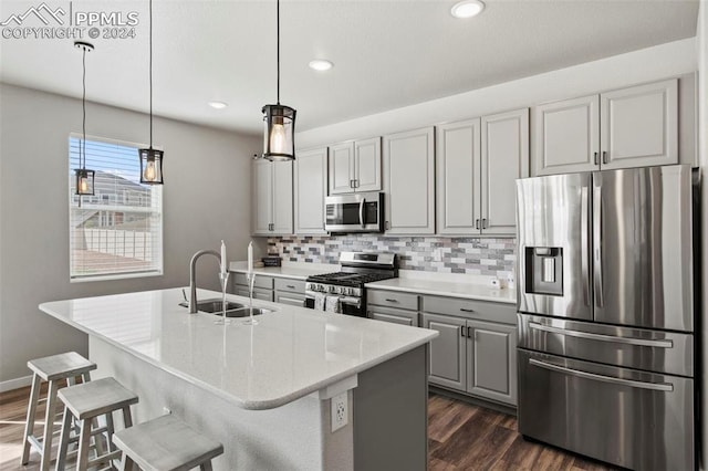 kitchen with appliances with stainless steel finishes, hanging light fixtures, gray cabinets, a center island with sink, and sink