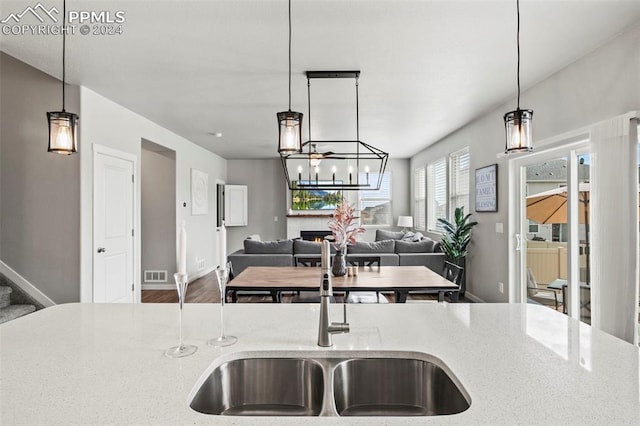 kitchen featuring hardwood / wood-style flooring, sink, an island with sink, decorative light fixtures, and light stone countertops