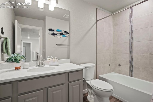 full bathroom with wood-type flooring, tiled shower / bath, vanity, and toilet