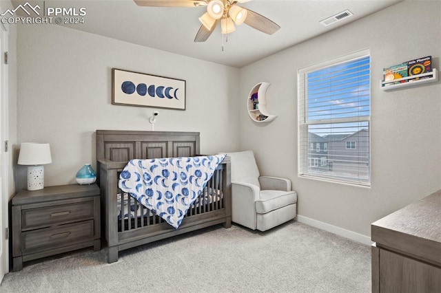 bedroom featuring light colored carpet, ceiling fan, and a nursery area