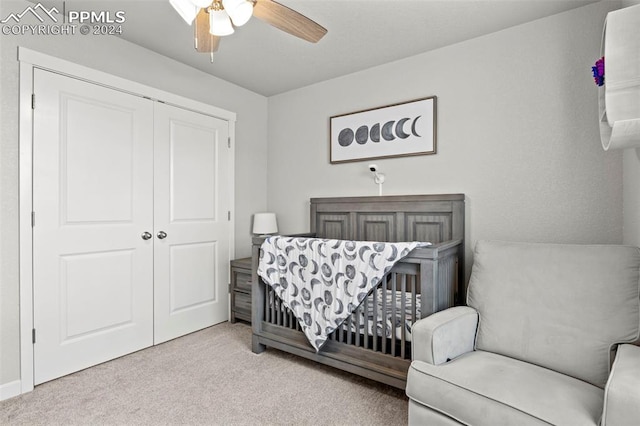 carpeted bedroom with ceiling fan, a nursery area, and a closet