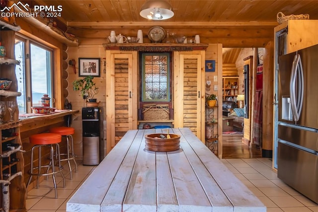 interior space with light tile patterned flooring, wood ceiling, stainless steel fridge, and log walls