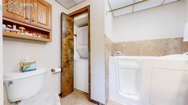 bathroom featuring a bathtub, stacked washer and dryer, toilet, and tile patterned floors