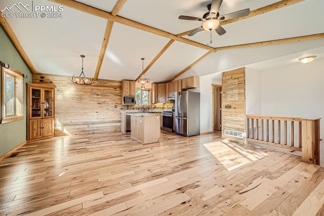 kitchen with vaulted ceiling with beams, hanging light fixtures, wood walls, a kitchen island, and appliances with stainless steel finishes