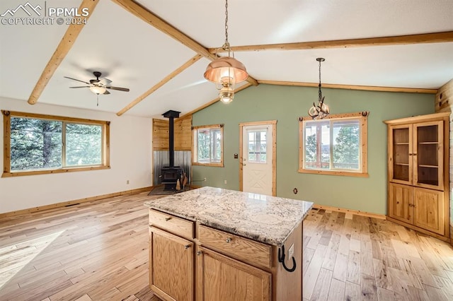 kitchen featuring ceiling fan, vaulted ceiling with beams, a wood stove, decorative light fixtures, and light hardwood / wood-style flooring