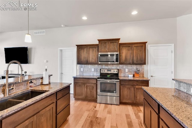 kitchen featuring appliances with stainless steel finishes, backsplash, light stone countertops, light hardwood / wood-style flooring, and sink