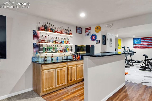 bar featuring sink, light hardwood / wood-style flooring, light brown cabinets, and black refrigerator