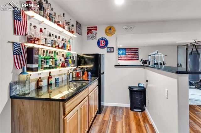 bar with light wood-type flooring, sink, and black fridge