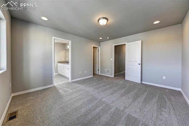 unfurnished bedroom featuring light carpet and ensuite bath