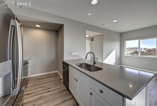 kitchen with sink, kitchen peninsula, white cabinetry, appliances with stainless steel finishes, and light wood-type flooring