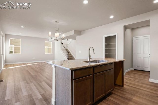 kitchen featuring an inviting chandelier, a kitchen island with sink, light hardwood / wood-style flooring, and sink