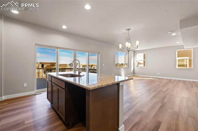 kitchen with sink, a center island with sink, a notable chandelier, light stone countertops, and light hardwood / wood-style floors