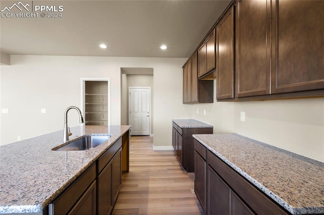 kitchen with light stone countertops, light hardwood / wood-style floors, a kitchen island with sink, and sink