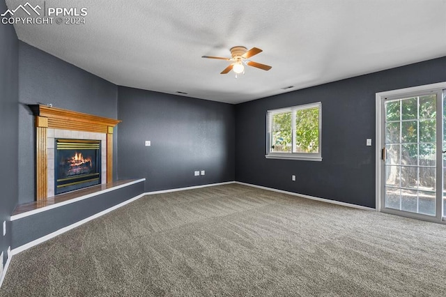 unfurnished living room with ceiling fan, a tile fireplace, carpet flooring, and a textured ceiling