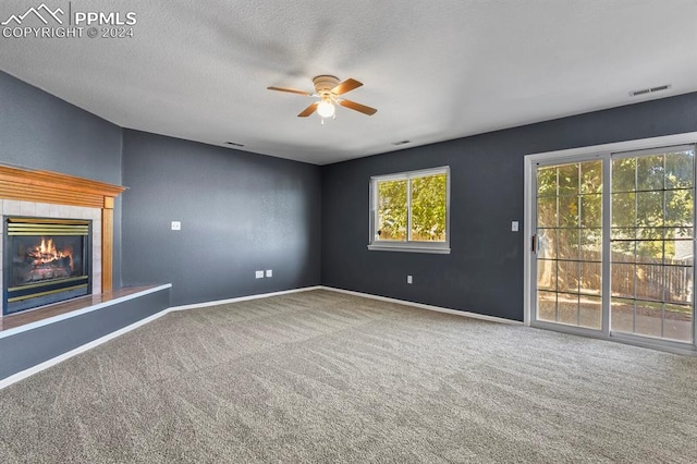 unfurnished living room featuring a textured ceiling, a tile fireplace, carpet, and ceiling fan