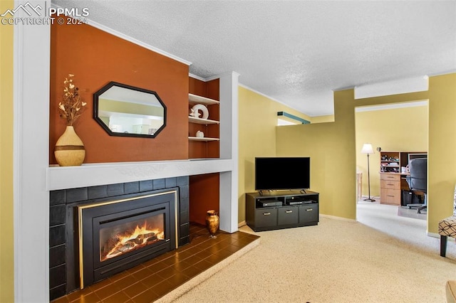 living room featuring built in shelves, a tiled fireplace, a textured ceiling, and crown molding