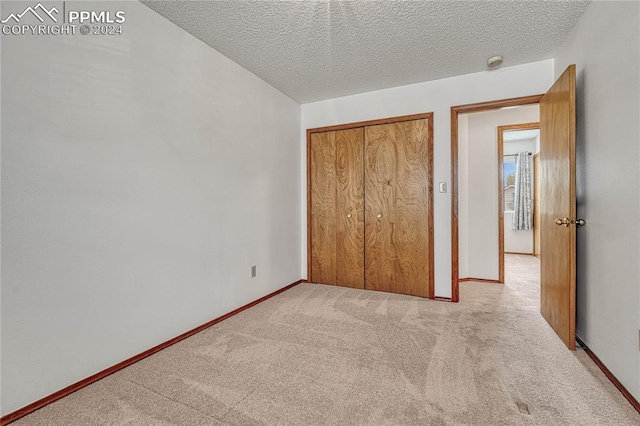 unfurnished bedroom featuring light carpet, a closet, and a textured ceiling