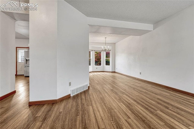 spare room featuring hardwood / wood-style floors, a textured ceiling, and a notable chandelier