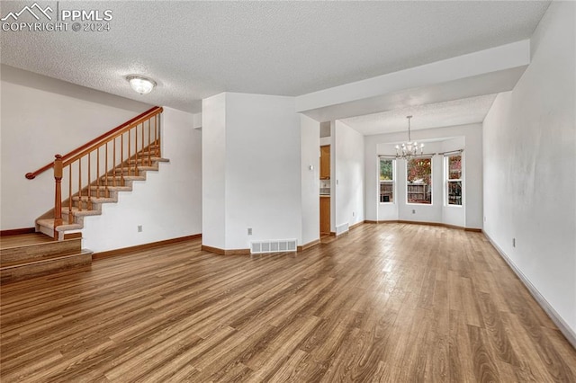 unfurnished living room with an inviting chandelier, a textured ceiling, and hardwood / wood-style flooring