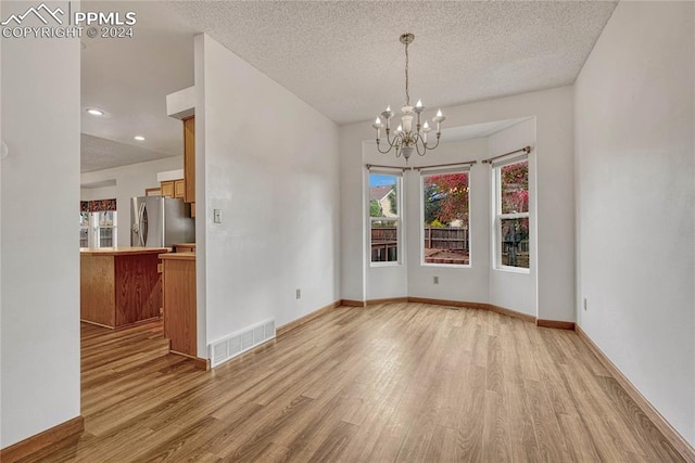 unfurnished dining area with plenty of natural light, light wood-type flooring, and an inviting chandelier