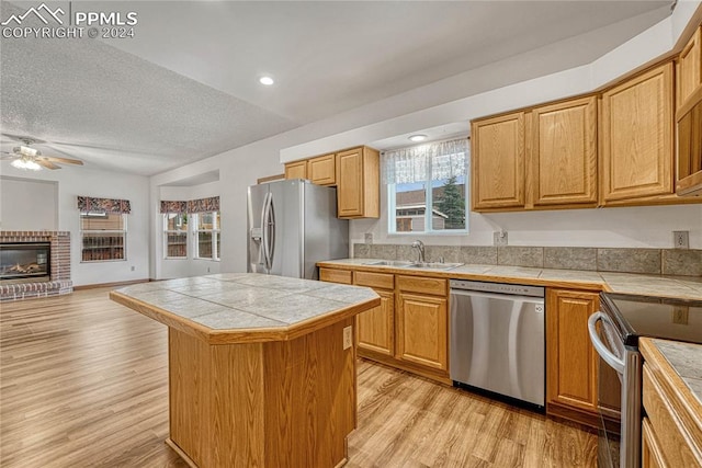 kitchen featuring sink, a center island, stainless steel appliances, light hardwood / wood-style flooring, and tile countertops