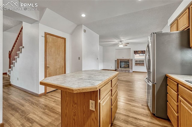 kitchen with a brick fireplace, light hardwood / wood-style flooring, stainless steel fridge, a textured ceiling, and a kitchen island