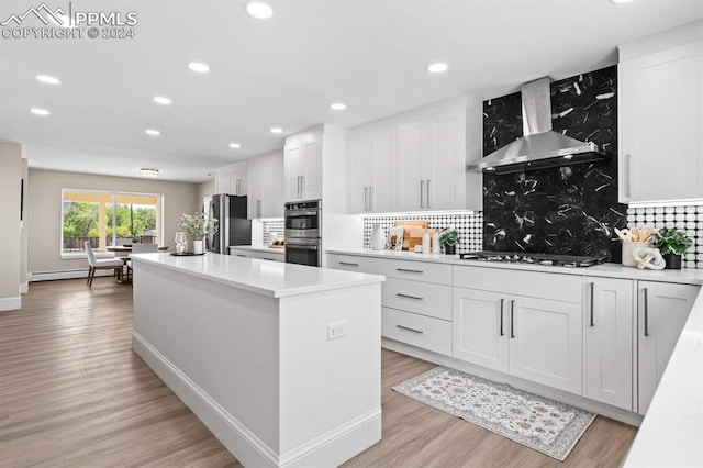 kitchen with a kitchen island, stainless steel appliances, wall chimney range hood, and white cabinetry