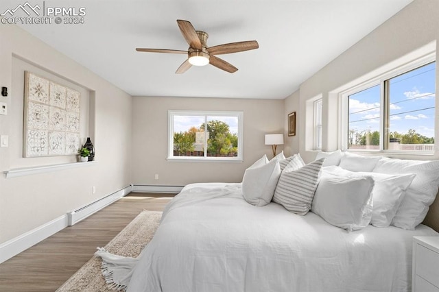 bedroom featuring a baseboard heating unit, multiple windows, hardwood / wood-style flooring, and ceiling fan