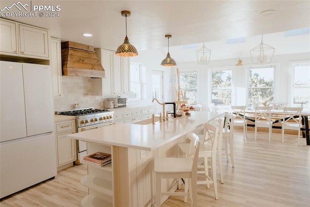 kitchen featuring premium range hood, stainless steel stove, decorative light fixtures, white fridge, and white cabinetry