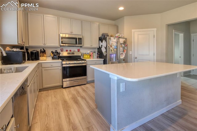 kitchen with appliances with stainless steel finishes, sink, a kitchen island, light hardwood / wood-style floors, and a breakfast bar