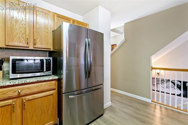 kitchen with light stone countertops, stainless steel appliances, tasteful backsplash, and light hardwood / wood-style flooring