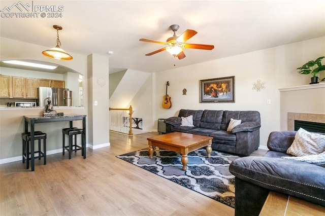 living room featuring ceiling fan, light hardwood / wood-style floors, and a tile fireplace