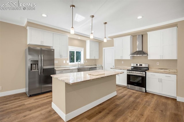 kitchen with appliances with stainless steel finishes, a kitchen island, decorative light fixtures, hardwood / wood-style floors, and wall chimney range hood