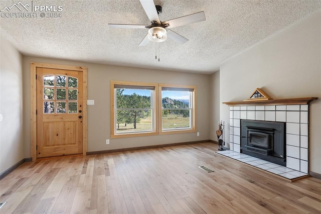 unfurnished living room with a textured ceiling, a tile fireplace, light hardwood / wood-style floors, and ceiling fan