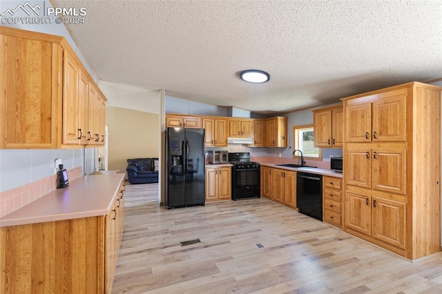 kitchen with a textured ceiling, black appliances, light hardwood / wood-style floors, and sink