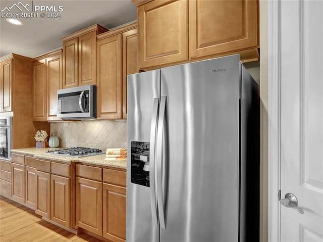 kitchen featuring tasteful backsplash, light hardwood / wood-style flooring, stainless steel appliances, and light stone counters