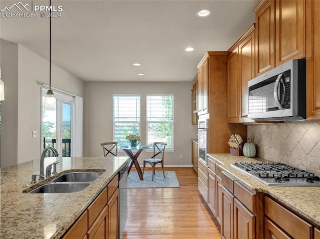 kitchen with pendant lighting, light stone countertops, sink, appliances with stainless steel finishes, and light wood-type flooring